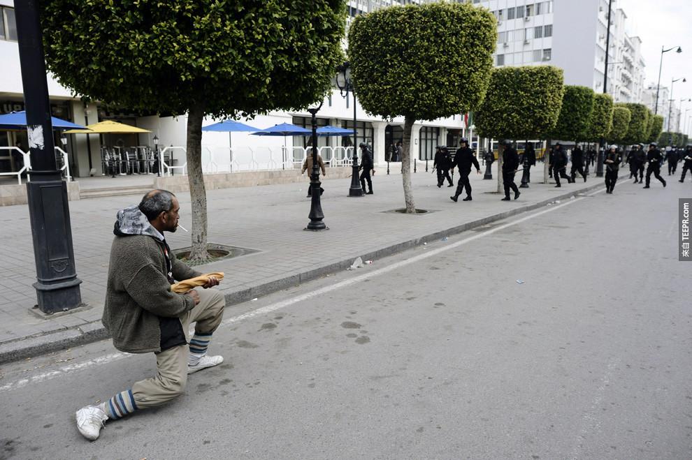 一名突尼西亚的民众拿着一个法国面包，敌档着警察的猛攻 (突尼西亚 2010)。