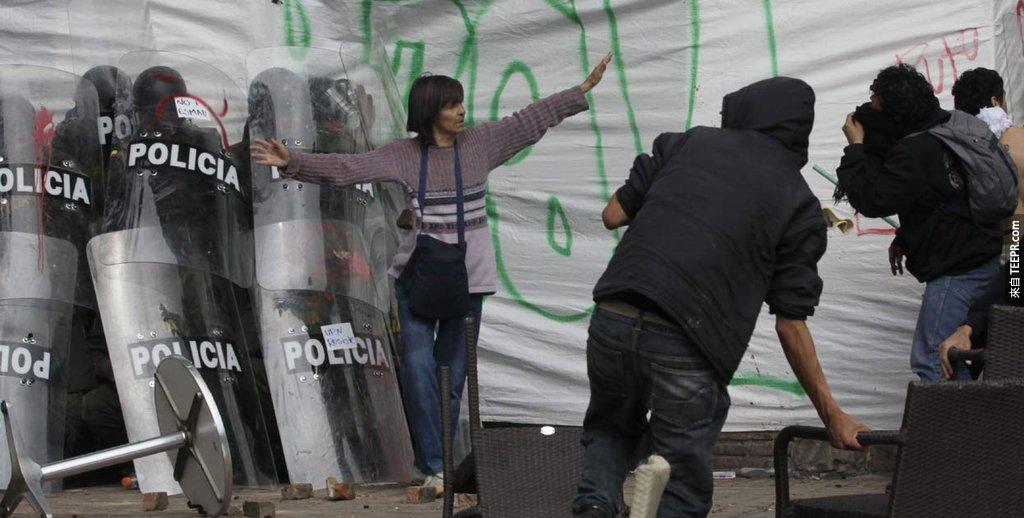 女性保护着一群被发狂的示威者逼到角落的警察 (波哥大，哥伦比亚 2011)。