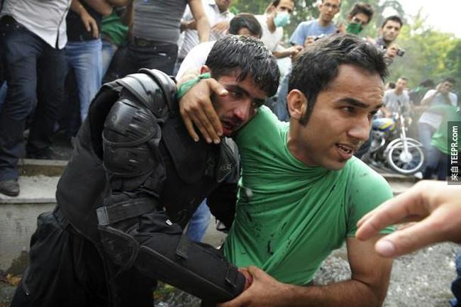 一位平民保护着一名被暴乱示威的群众打伤的警察 (伊朗德黑兰 2009)。
