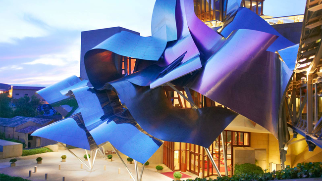 This hotel's colorful, fabric-like design was created by architect Frank Gehry. It was made from silver, gold, and pink titanium. The building's unconventional style makes it a work of art itself. It's located in the north of Spain, in the Basque country.