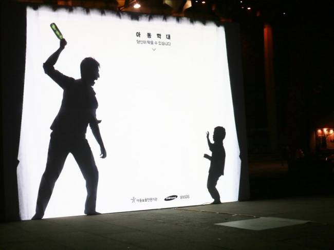 在一個投影螢幕上，一個憤怒的爸爸正要拿著酒瓶攻擊他年幼的兒子。