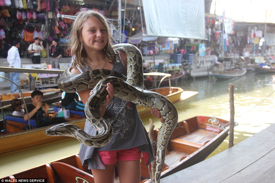 The family visited Thailand as part of their round-the-world trip, pictured is Lili Mai holding a snake at a market in Bangkok