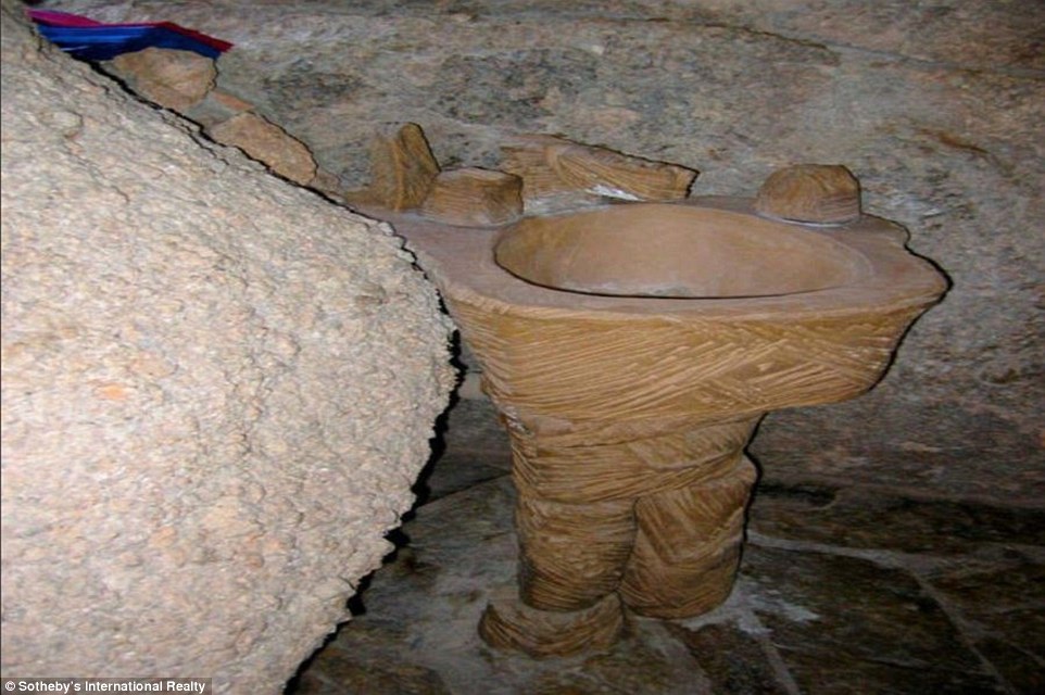 A bathroom in the house appears to have walls made from boulder and a unique sink, that seems to be made out of another type of rock or stucco substance