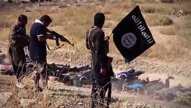 Extremists holding the ISIS flag and machine guns stand over a group of prisoners forced to lie in the dirt