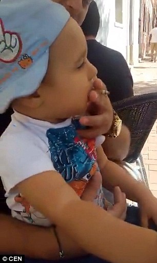 The video, thought to have been taken outside a cafe in Spain, shows the little boy sitting on a man's lap and drinking from a glass of alcohol