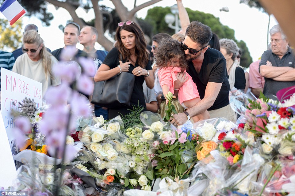 A man hugs a young child as he leans down to lay a flower on the pile of tributes to the scores of people who died in the massacre