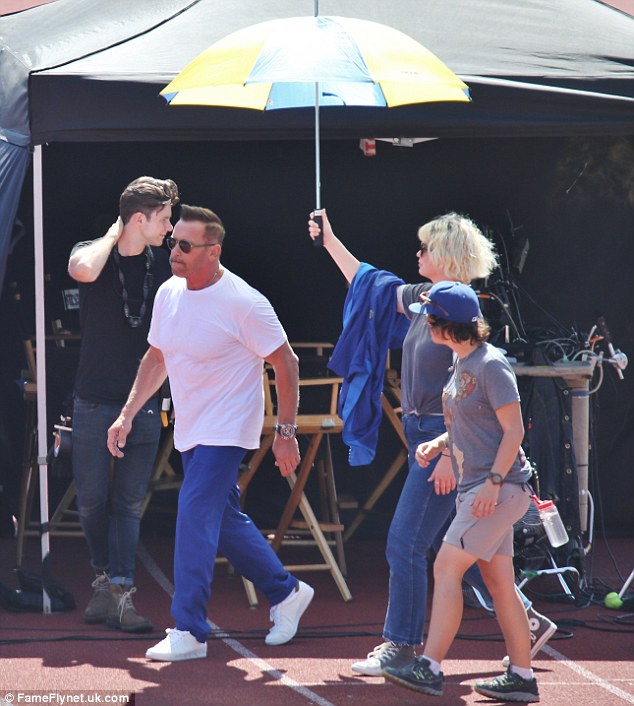 At your service: In between, Arnold took off his jacket to cool down in the heat while a member of the production crew shielded him further from the rays with an umbrella