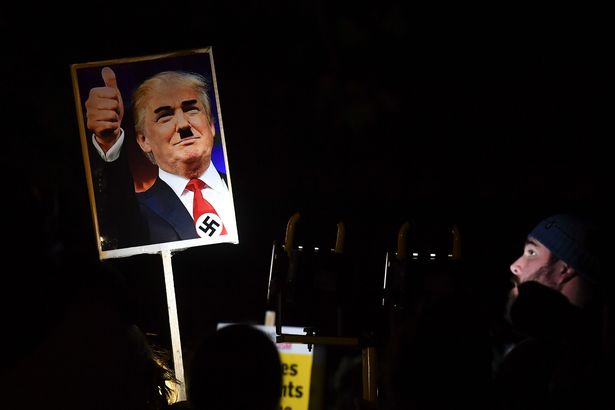 A demonstrator holds a placard showing a picture of US President-elect Donald Trump modified to add a swastika