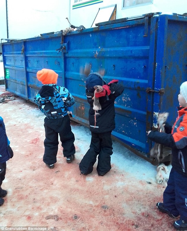 The children chuck the severed hooves into a rubbish container while standing on the blood stained snow  