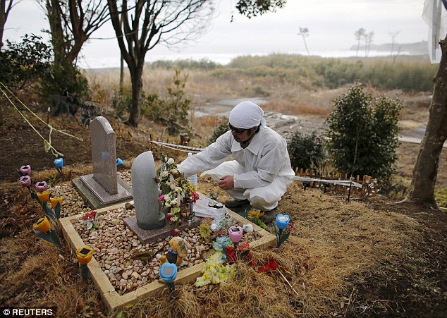 Mr Kimura places a wreath at the grave of his family, where he hopes to one day place his daughter's body