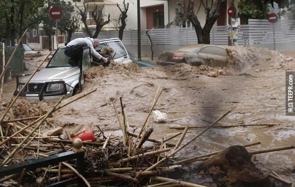 在二月的希腊雅典洪水灾害道路现场，一位英勇的男士救出因为洪水而被卡在车内的女士。