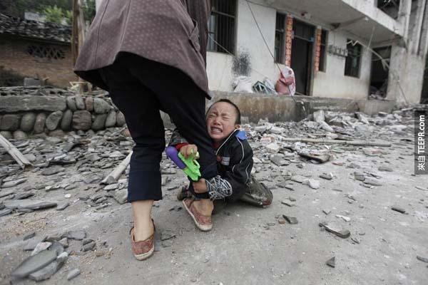 在中国四川地震余波中，一名小男孩紧紧抓住母亲的大腿哭泣。