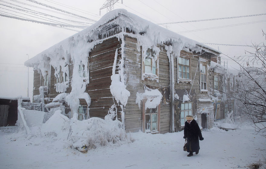 一名妇人走过村中一幢被冰雪覆蓋的小屋。
