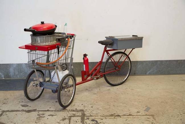 This bike has a tiny stove attached to the front, a fire extinguisher for safety, and storage for food in the back.