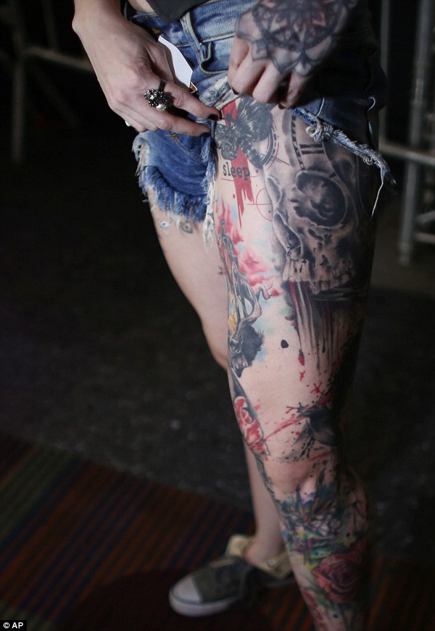 This woman hitches up her jeans to show of the design on her left leg, pictured which includes a skull