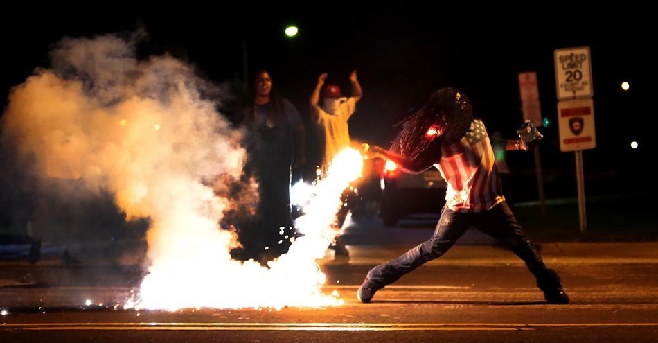 12. 在麦可·布朗枪击案抗议当中，一位示威者正丢回催泪瓦斯。