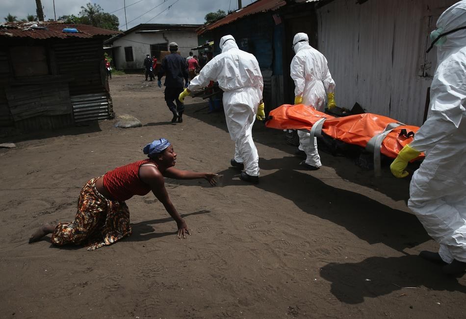  3. 一個女子正在爬向她姊妹的屍體，伊波拉病毒掩埋團隊正在將屍體抬走。