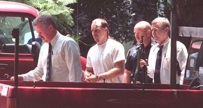 Hank Carr (center), who later used a hidden key to escape incarceration and murdered the two detectives on the left and far right. Carr then led cops on a high-speed chase before being killed in a standoff.