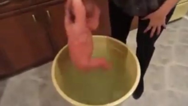 The video shows a baby being held upside down by her legs and being repeatedly submerged in a bucket of water.