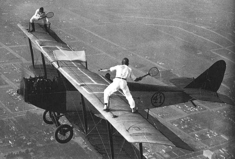 Two men in 1920, playing tennis on the wings of a bi-plane.