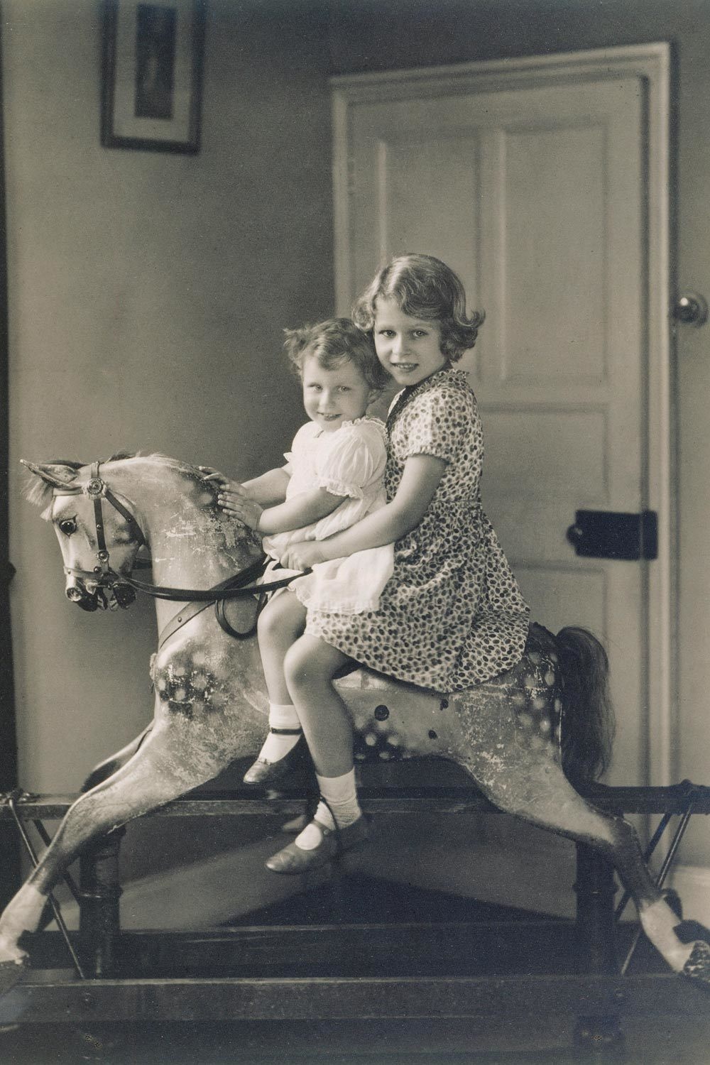 A very early photo of Princess Elizabeth and Princess Margaret, riding their rocking horse.