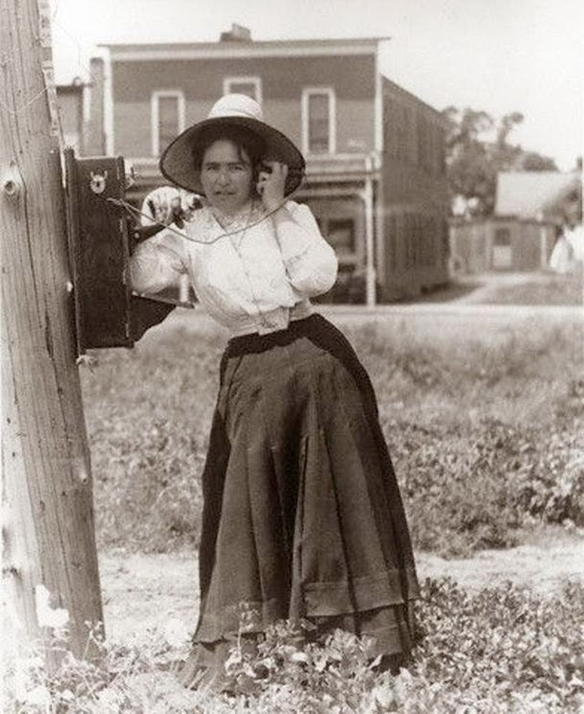 A woman chatting on a hand crank telephone.
