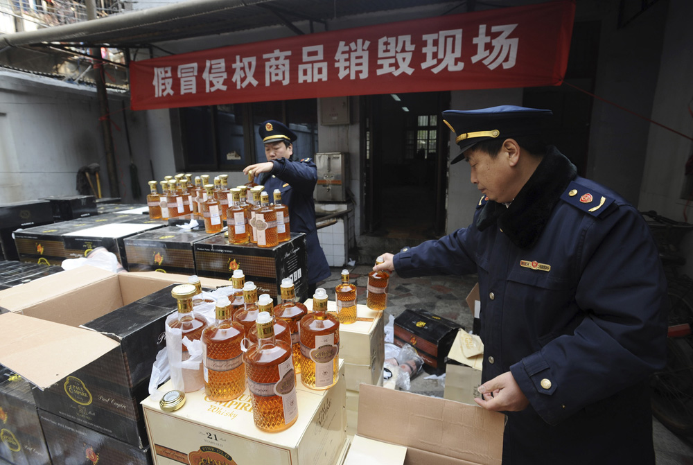 Commercial law enforcement personnel examine bottles of confiscated fake whisky before pouring it into sewage during a massive destruction campaign of fake products in Wuhan