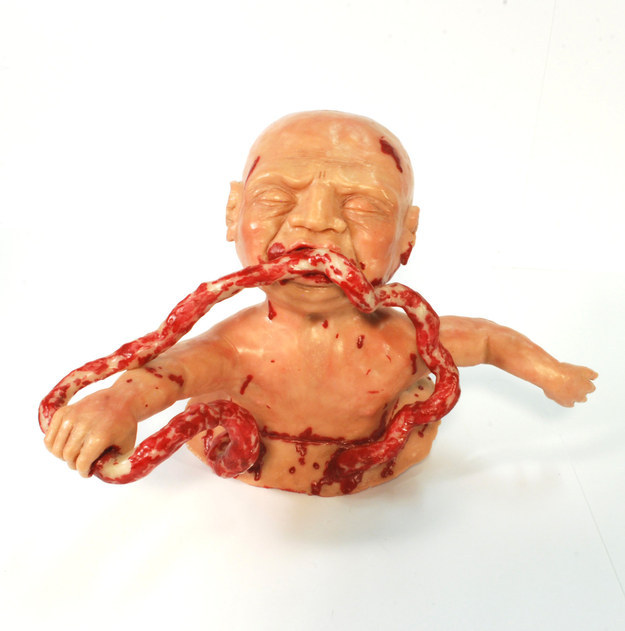 A horrific sculpture of a zombie baby eating its own umbilical cord.