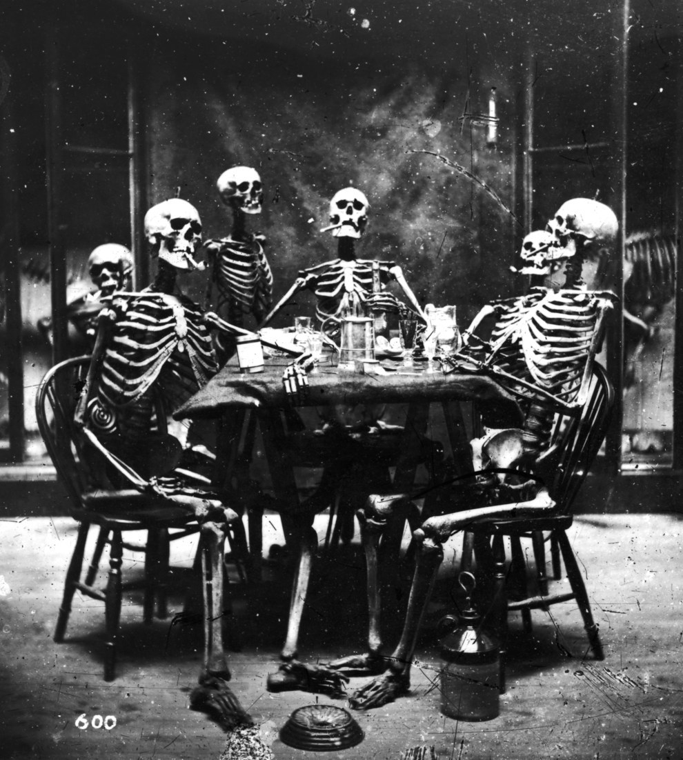 Six skeletons smoking around the dinner table, circa 1865.