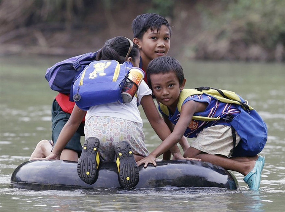 Elementary school students cross a river on inflated tire tubes to school in Rizal Province, Philippines.
