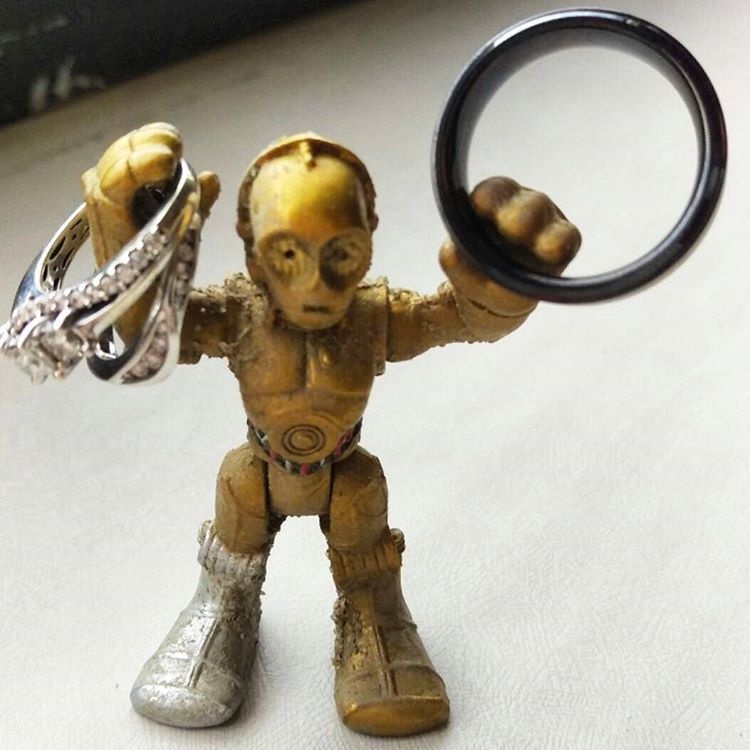 A mini C-3PO holding all the wedding bands found on the beach. 