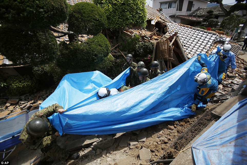 Heroes: Rescue workers carry Yumiko Yamauchi, 93, on a stretcher covered in a blue plastic sheet, as they tread their way through broken tiles from a toppled house in Mashiki