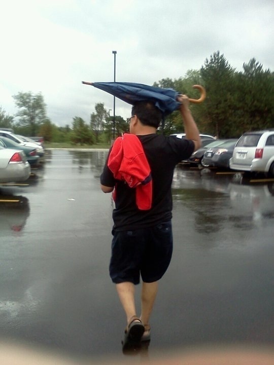 He keeps getting wet despite the umbrella.