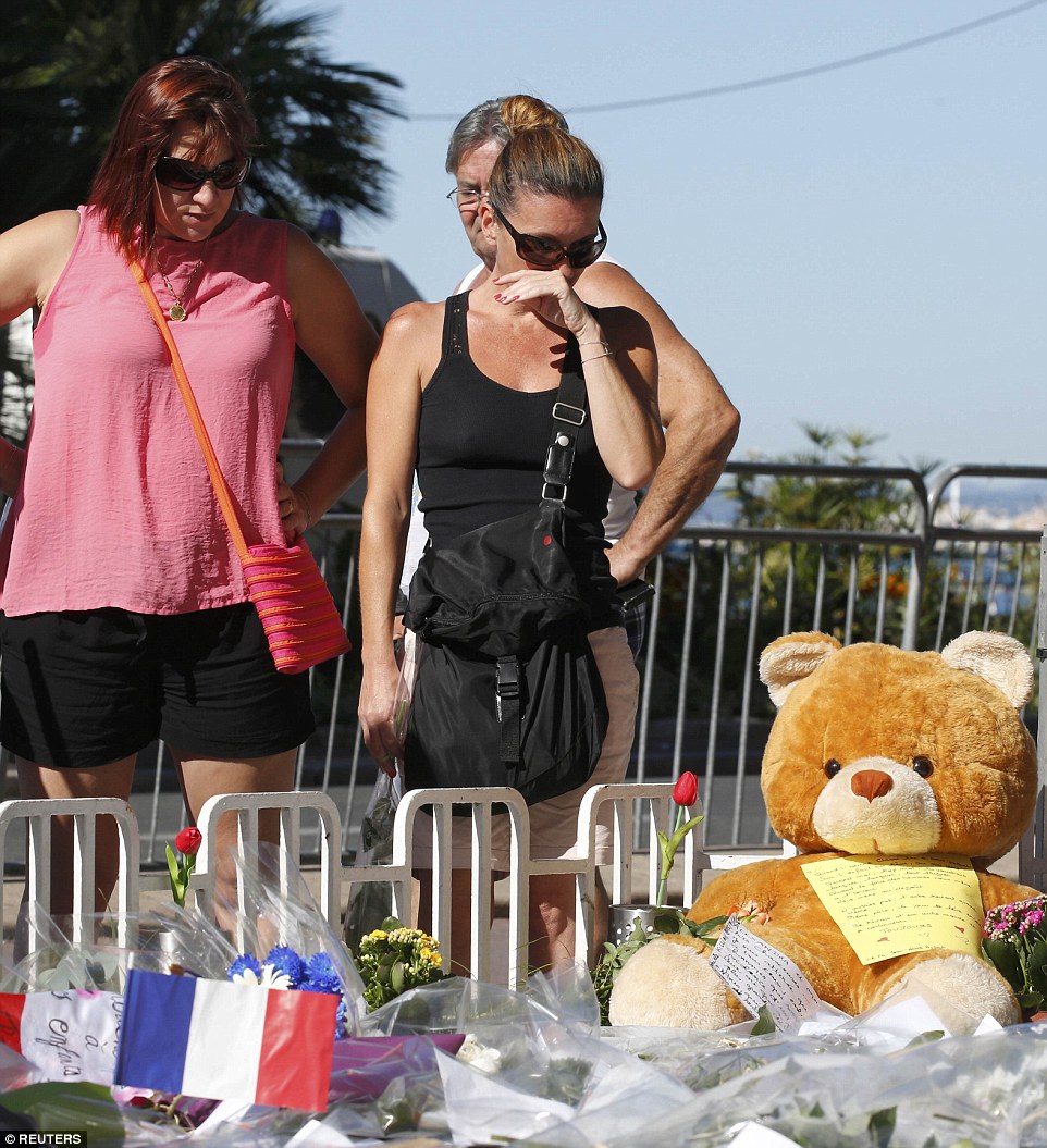 A woman cries at a memorial honouring the dead, where hundreds of people have lit candles and laid flowers, a teddy bear was also left