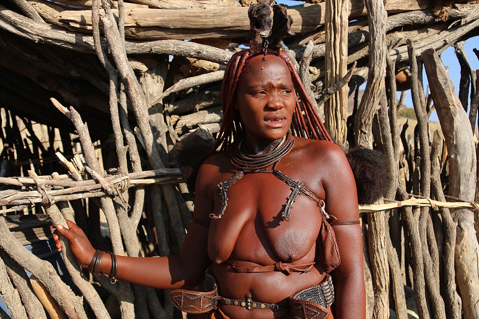 A woman stands in front of a fence in the breathtaking rural setting in Namibia which is home to the Himba tribe