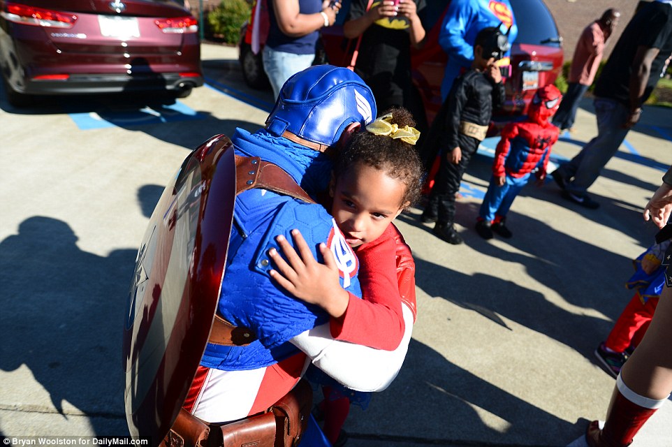 A young girl is hugged by a man dressed as Captain America at the superhero-themed funeral for six-year-old Jacob Hall 