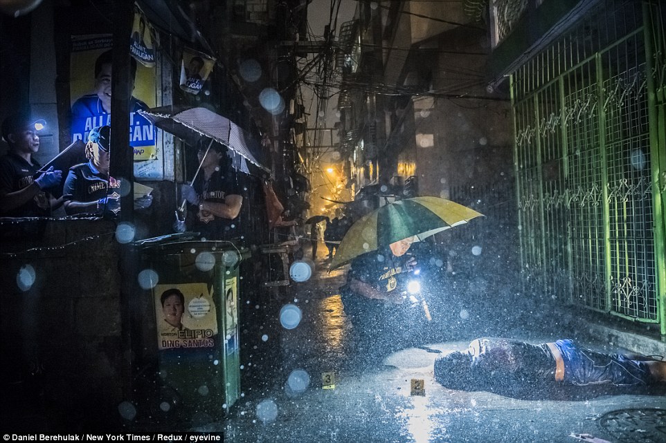 Police investigators hunched over the body of Romeo Torres Fontanilla, who was gunned down, witnesses said, by two unknown men on a motorbike, as it rains in the Pasay district of Manila, Philippines