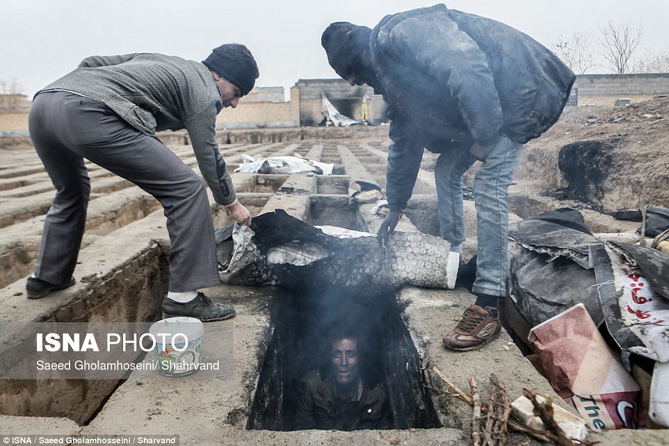 A man pictured living in an empty grave to escape freezing temperatures in Iran, where unemployment stands at around 12 per cent